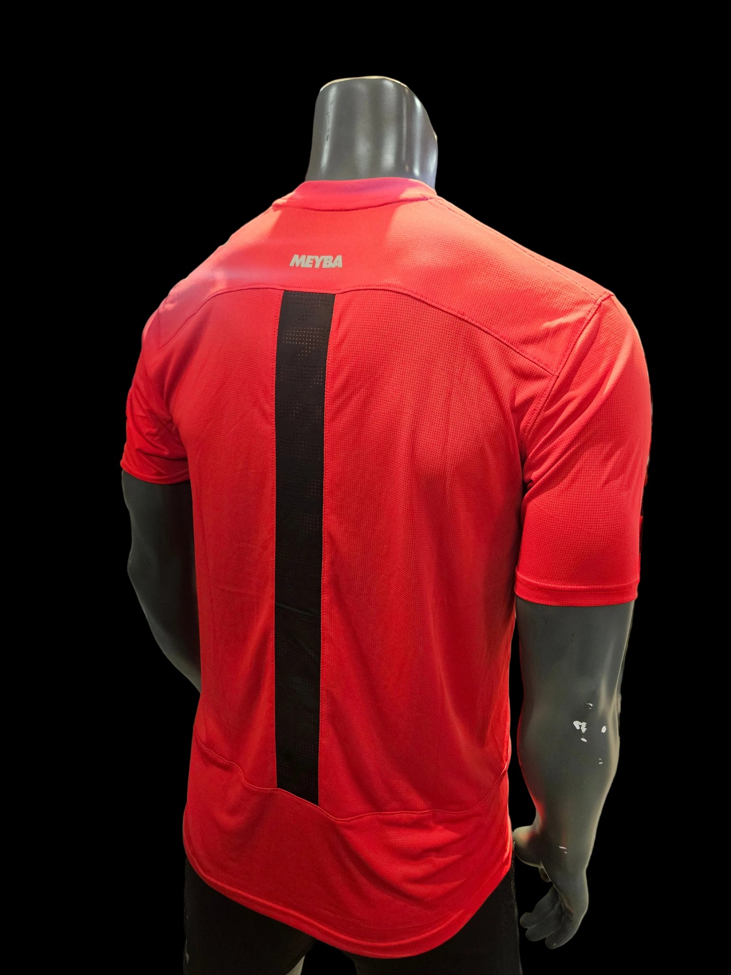 A red athletic short-sleeve shirt with a wide black horizontal stripe across the back, displayed on a black mannequin torso inside a retail store.