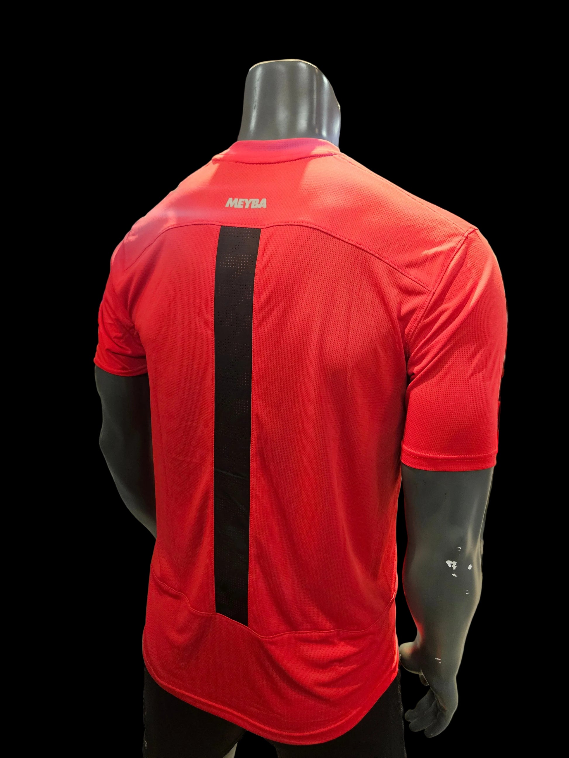 A red athletic short-sleeve shirt with a wide black horizontal stripe across the back, displayed on a black mannequin torso inside a retail store.